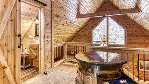 Un interior de madera con techo inclinado, una mesa redonda con cubierta de vidrio y una ventana con vistas a árboles.