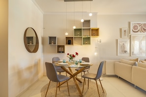 Ein modernes Wohnzimmer mit einem Esstisch mit Glasplatte, vier Stühlen, einem Sofa und einem Couchtisch.