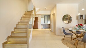 A modern interior with a wooden staircase, a dining area with a round table and chairs, and a kitchen in the background. - Something special in Chalkida - 300 m from the seafront (Xirovrisi)