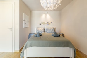 Ein modernes Schlafzimmer mit einem großen Bett, einer Kristallleuchtre und einer Reihe gerahmter Bilder an der Wand.