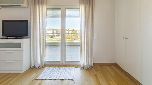 A room with a sliding glass door leading to a balcony, a flat-screen TV on a white cabinet, and a wooden floor. - Something special in Chalkida - 300 m from the seafront (Xirovrisi)
