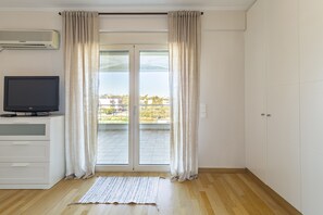 Une pièce dotée d’une porte-fenêtre coulissante donnant sur un balcon, d’un téléviseur à écran plat posé sur un meuble blanc et d’un plancher en bois.