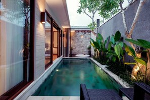 Un área de piscina exterior moderna con un muro de piedra, un pequeño elemento acuático y abundante vegetación.