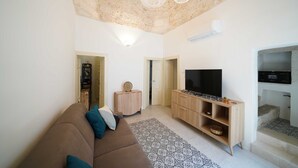 Ein Wohnzimmer mit einem braunen Sofa, einem Fernseher auf einem Holzboden, einem gemusterten Teppich und einer Steindecke.