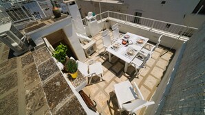 Eine Dachterrasse mit Esstisch, Stühlen, einem Blumentopf und einer dekorativen Vase.