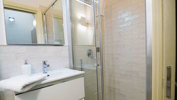 Un bagno moderno con doccia vetrata, un lavandino bianco con uno specchio sopra e un pavimento piastrellato.