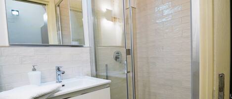 Une salle de bain moderne avec une douche à parois de verre, un lavabo blanc avec un miroir au-dessus et un sol carrelé.