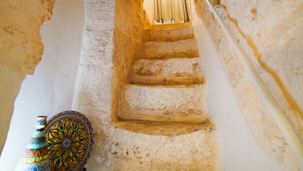 Eine schmale Steintreppe mit Licht oben, die zu einer höheren Ebene führt.
