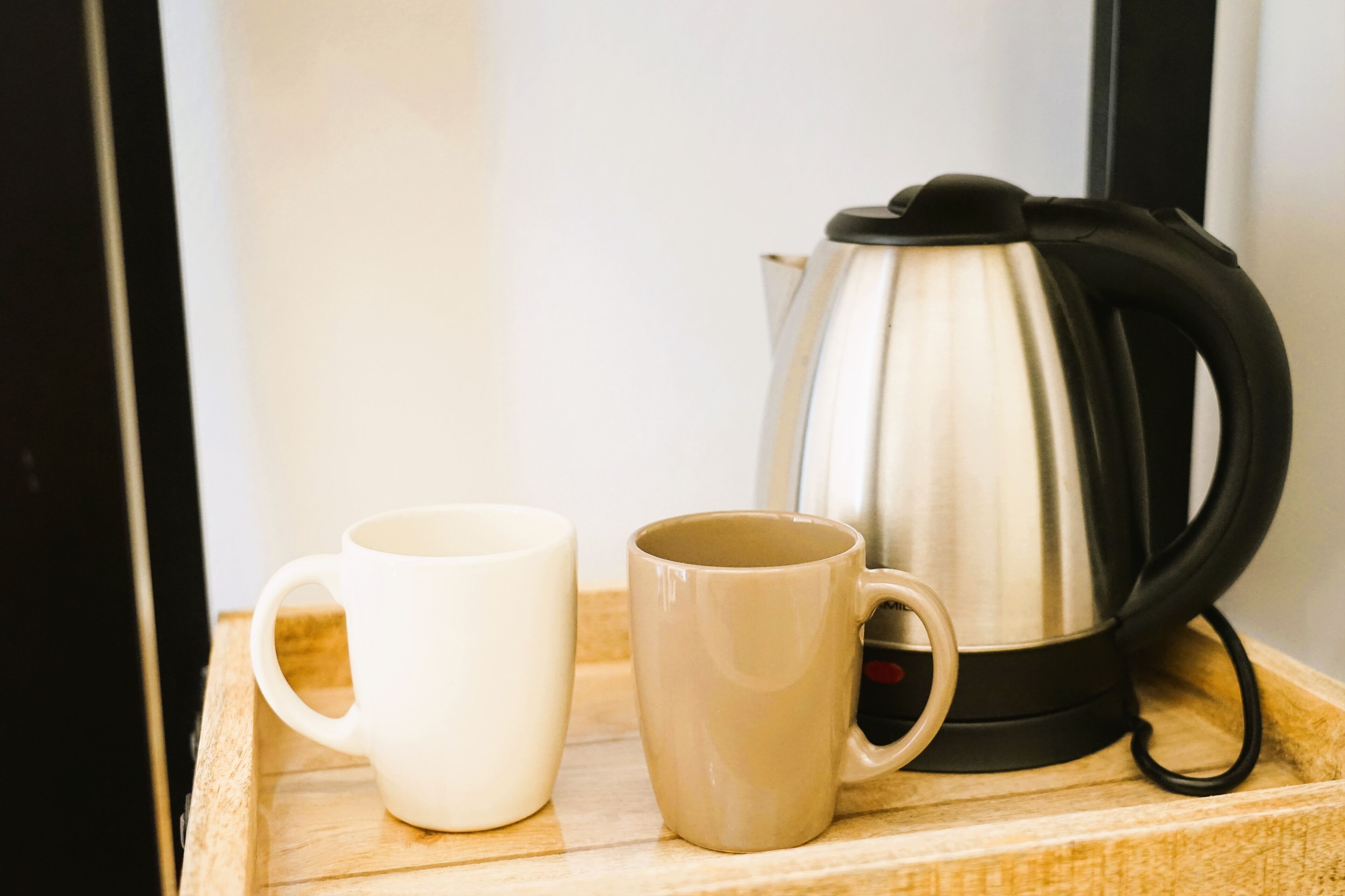 A wooden tray with two mugs and a stainless steel electric kettle.