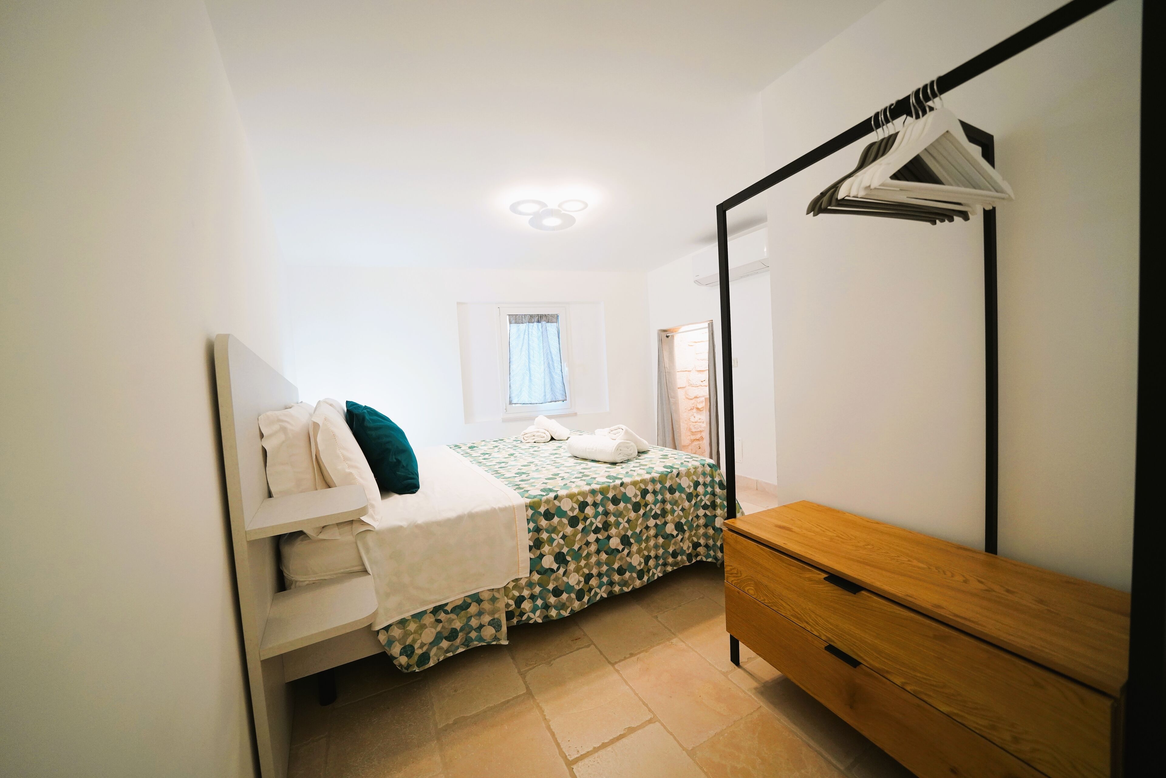 A bedroom with a bed, a wooden dresser, a mirror, and a window with curtains.