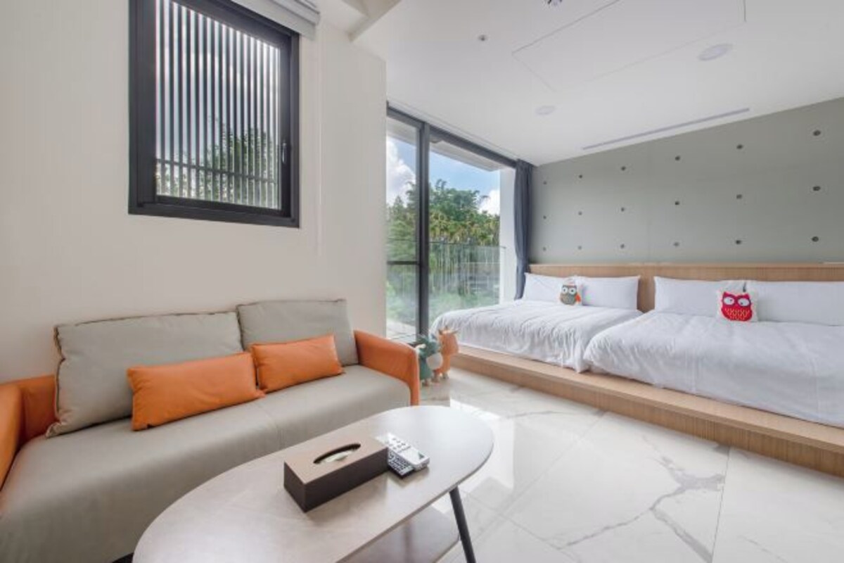 Una habitación de hotel moderna con un sofá, una cama con cabecera, una mesita y una ventana con persianas.