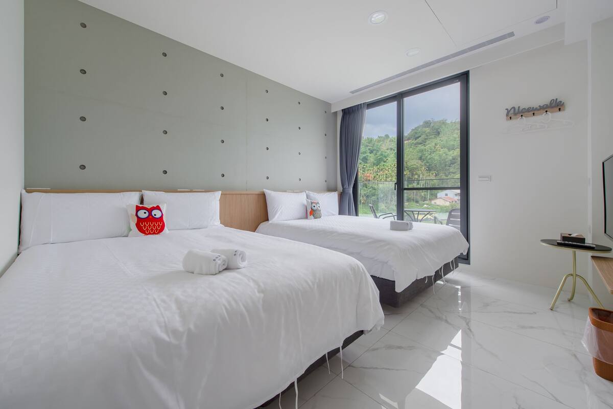 A hotel room with two beds, a large window with a view, a flat-screen TV, and a small table.