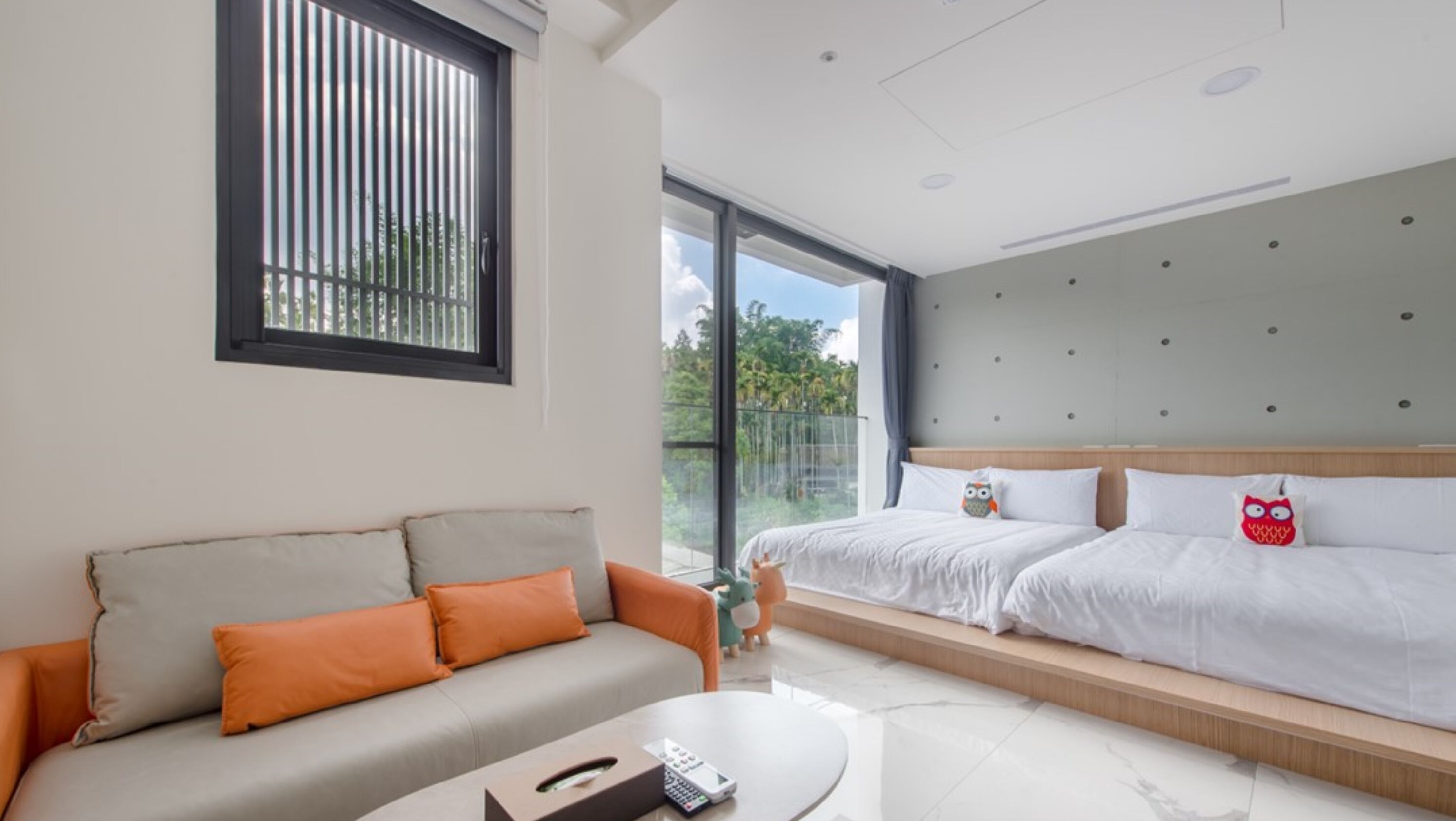 Habitación de hotel moderna con sofá, cama con dos almohadas, una mesita y un ventanal grande con vistas a zonas verdes.