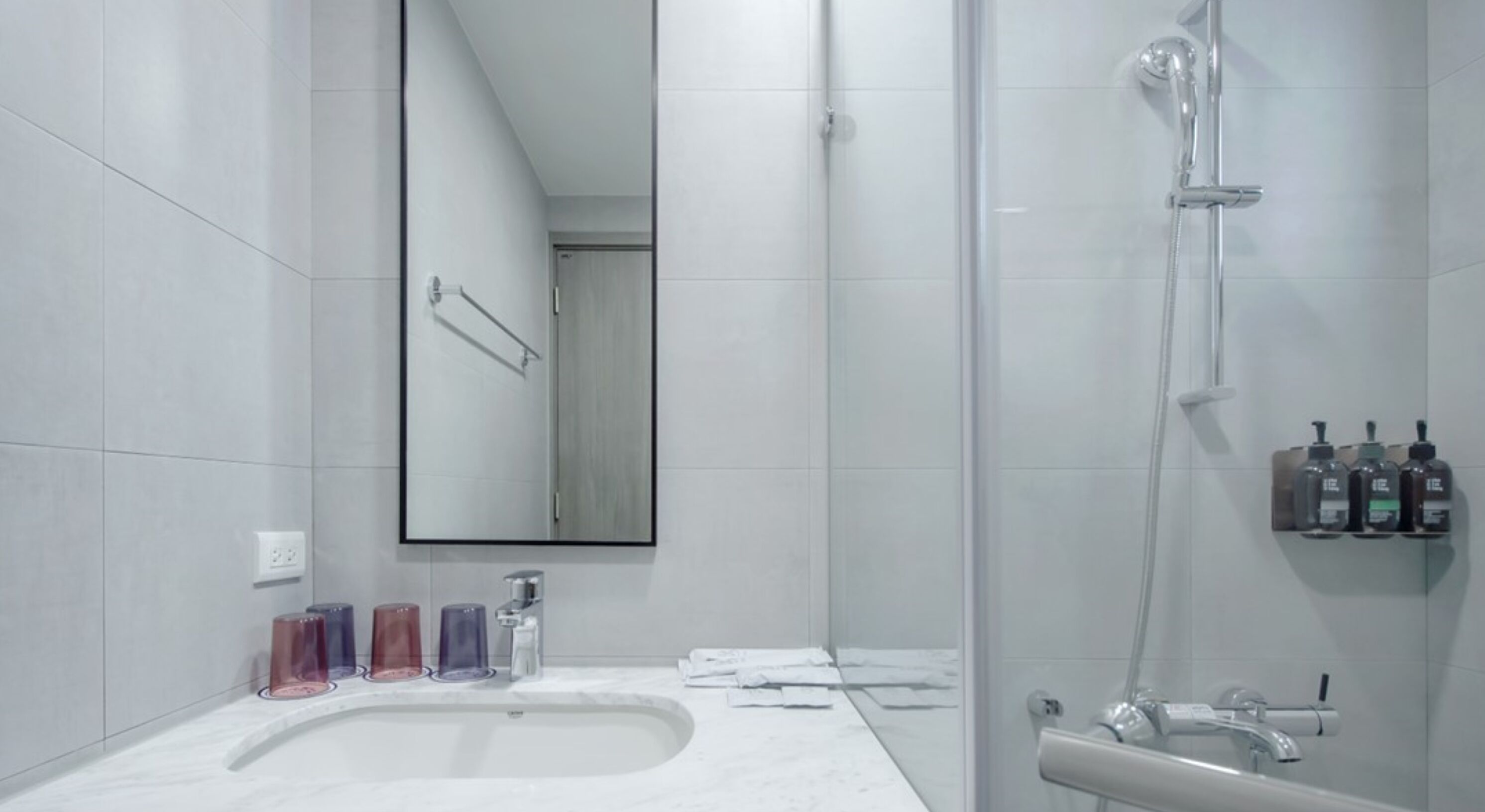 A modern bathroom with a large mirror, a shower, and a sink with soap dispensers.