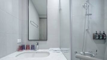 A modern bathroom with a large mirror, a shower, and a sink with soap dispensers.