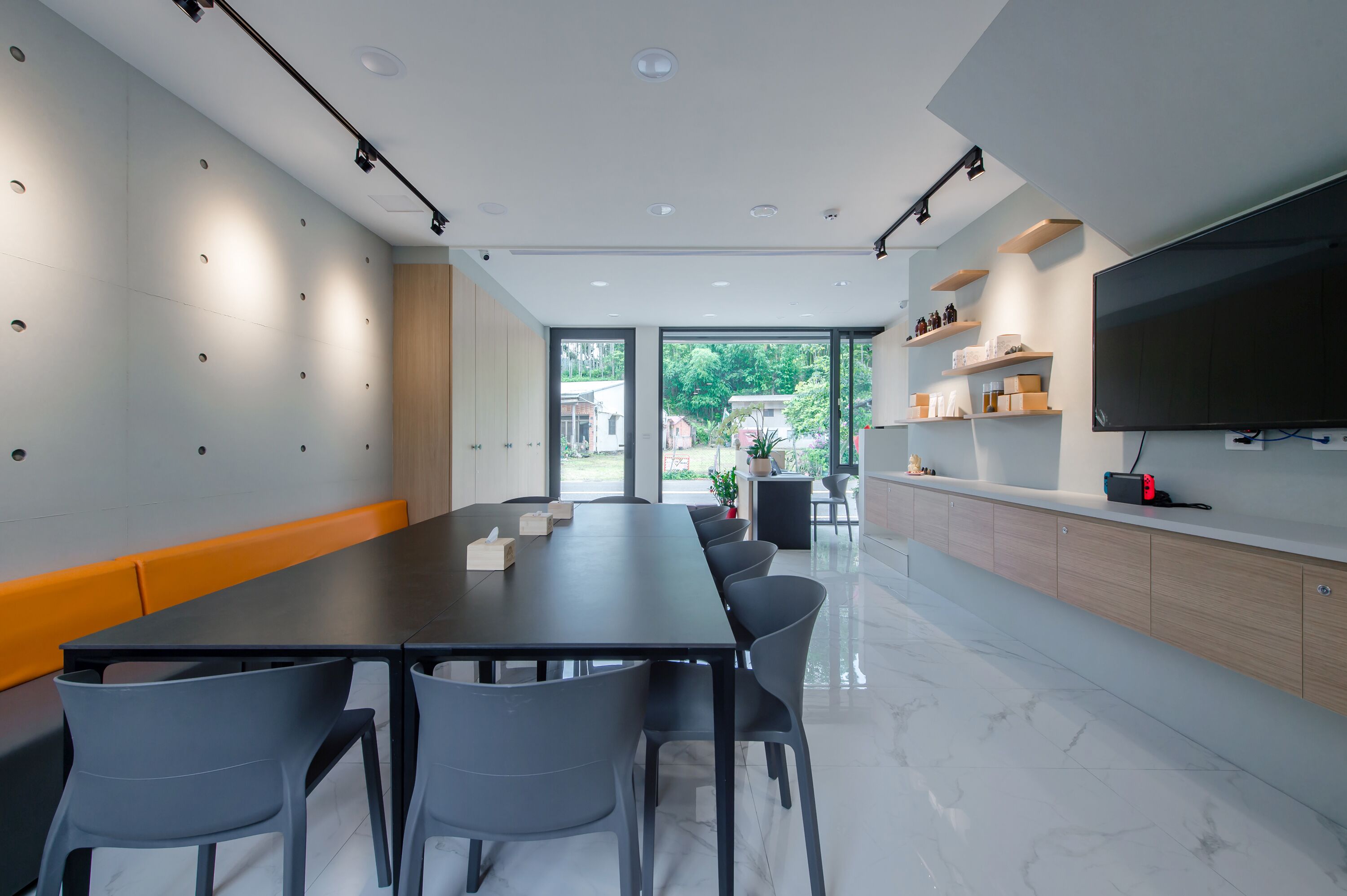 A modern conference room with a long table, chairs, a TV, and a view of the outdoors.