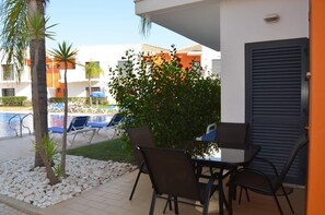 Relax by the pool with lounge chairs and a small table for al fresco dining amidst lush greenery.