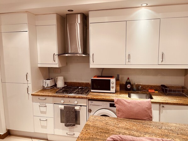 Compact kitchen with stainless steel range hood, microwave, toaster, and washing machine.