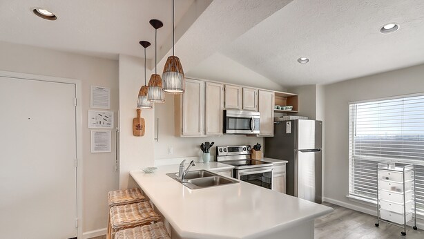 A modern kitchen with white cabinetry, stainless steel appliances, and a central island with bar stools. - Salty Moose | 2BD Close To Whitecap Beach | Pool (Corpus Christi)