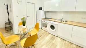 A modern kitchen with white cabinets, a built-in oven, a washing machine, and a dining area with yellow chairs. - China Town Madrid 02 (1-bedroom apartment) (Madrid)