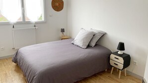 A bedroom with a bed, a nightstand, a lamp, a radiator, and a window.