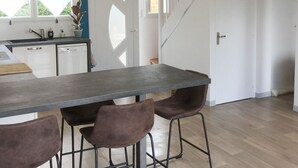 A modern kitchen with a long countertop, four chairs, and a staircase leading to another room.