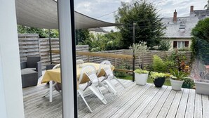 An outdoor patio with a table and chairs, surrounded by potted plants and a wooden fence.