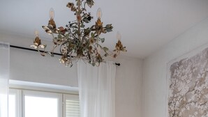 Une chambre avec un grand lit, un lustre, une table de chevet avec une lampe et une vue sur l’extérieur par une porte.