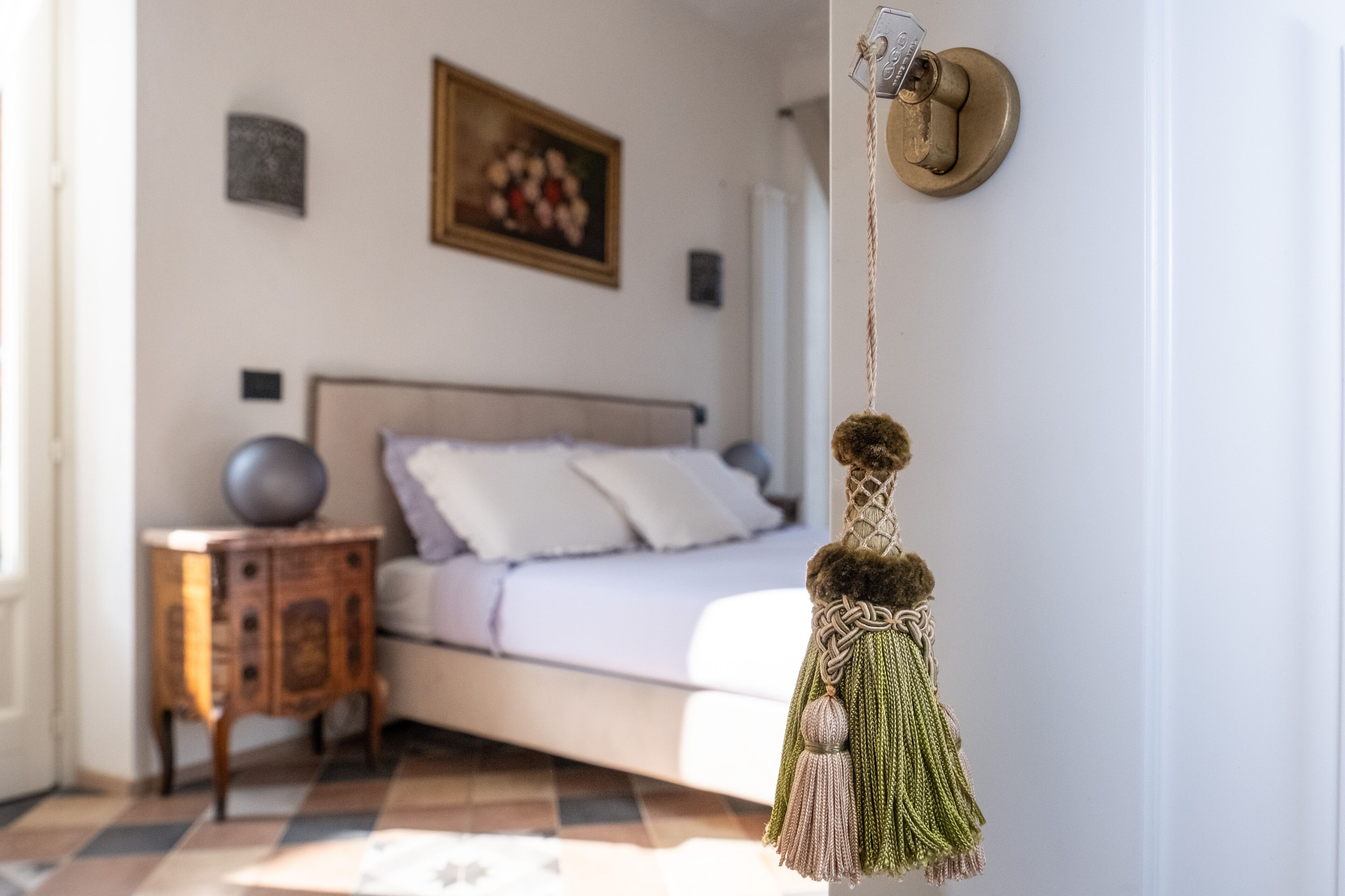 A bedroom with a bed, a nightstand, a wall-mounted macrame key holder, and a painting on the wall.