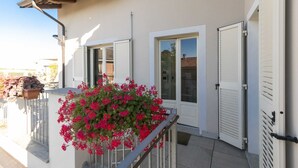 Un bâtiment aux murs extérieurs blancs, doté d’un balcon avec une rambarde en métal et d’un pot de fleurs contenant des fleurs rouges.