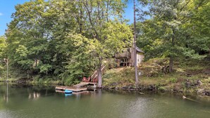 A cabin by a lake with a dock and chairs. - Black Rapids Retreat | Waterfront Cozy Cottage (Leeds and the Thousand Islands)