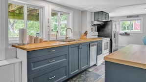 A modern kitchen with grey cabinets, a wooden countertop, a stainless steel sink, and a built-in oven. - Black Rapids Retreat | Waterfront Cozy Cottage (Leeds and the Thousand Islands)