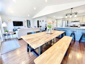 Eine moderne Küche mit Holzarbeitsplatten, einem Essbereich mit großem Holztisch und Bänken sowie einer sichtbaren Kücheninsel mit Barhocker.