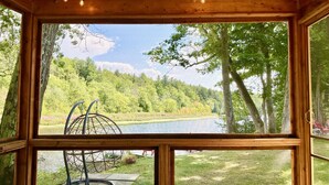 A wooden cabin with a large window overlooking a lake surrounded by trees. - The Riverside Retreat | Beach, Kayaks, Fire Pit (Gananoque)