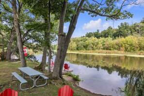 Area pic-nic sul lago con tavolo e sedie, circondata da alberi e vista sul lago.