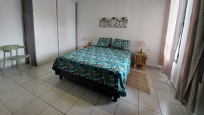 Un dormitorio con una cama, dos mesitas de noche, una lámpara colgante, una silla y una obra de arte en la pared.
