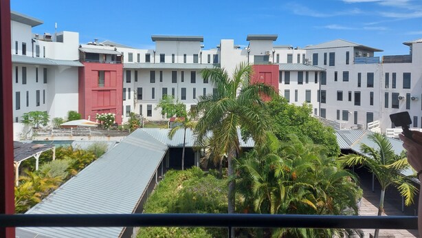 Un edificio moderno con varios pisos, que presenta una combinación de fachadas blancas y rojas, rodeado de abundante vegetación.