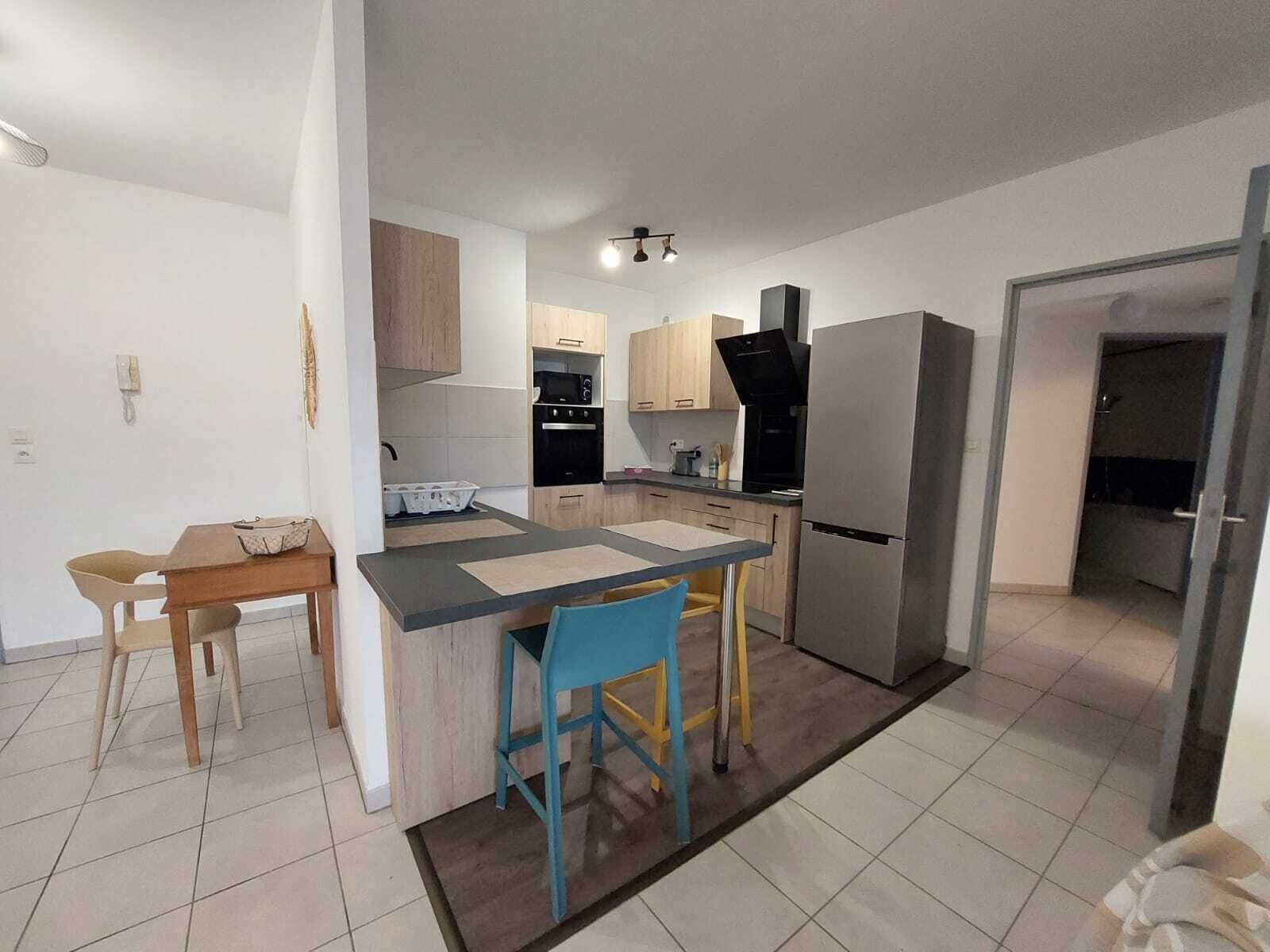 Une cuisine compacte dotée d’un îlot central, d’un coin repas avec deux chaises et d’un réfrigérateur.