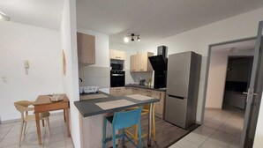 Una cocina compacta con una isla central, una zona de comedor con dos sillas y un refrigerador.