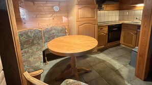 A wooden interior with a round wooden table and chairs, a clock on the wall, and a kitchen area with cabinets and appliances. - Ferienwohnung im Holzhaus, 5-10 Min. vom Schönen Wandlitzsee Entfernt (Wandlitz)