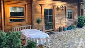 A wooden cabin with a covered patio, a table with a floral tablecloth, and potted plants. - Ferienwohnung im Holzhaus, 5-10 Min. vom Schönen Wandlitzsee Entfernt (Wandlitz)