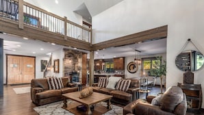 A spacious living area with leather sofas, a coffee table, and a fireplace. A wooden staircase leads to an upper level. - 1PM Check In/Out | Scenic Mountain Cabin! Private Setting+Spa/Epic GameRm (Ronald)