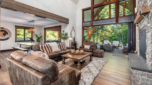 A spacious living room with leather sofas, a wooden coffee table, and large windows offering a view of the outdoors. - 1PM Check In/Out | Scenic Mountain Cabin! Private Setting+Spa/Epic GameRm (Ronald)