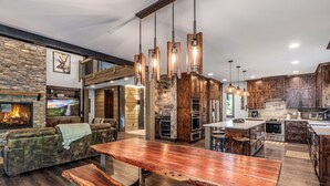 A spacious kitchen with wooden cabinets, a large island, and a stone fireplace. - 1PM Check In/Out | Scenic Mountain Cabin! Private Setting+Spa/Epic GameRm (Ronald)
