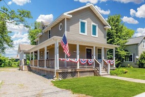 Une maison à deux étages avec un porche, des drapeaux américains et une pancarte indiquant « Bienvenue ».