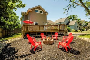 Un jardin avec un foyer, des chaises rouges et une terrasse en bois.