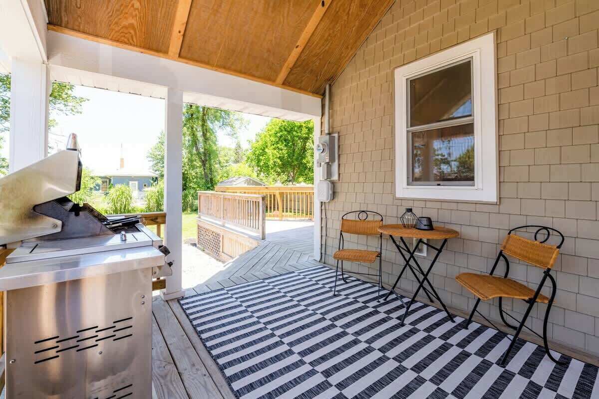 A covered patio with a grill, two tables with chairs, and a view of the backyard.