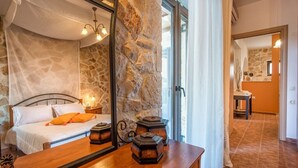 Een slaapkamer met een stenen muur, een bed met witte beddengoed, een houten dressoir en een grote spiegel.
