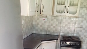 A kitchen with a refrigerator, stove, white cabinets, and tiled backsplash. - Garden Guest House Bed & Bre Chitungwiza (Harare)