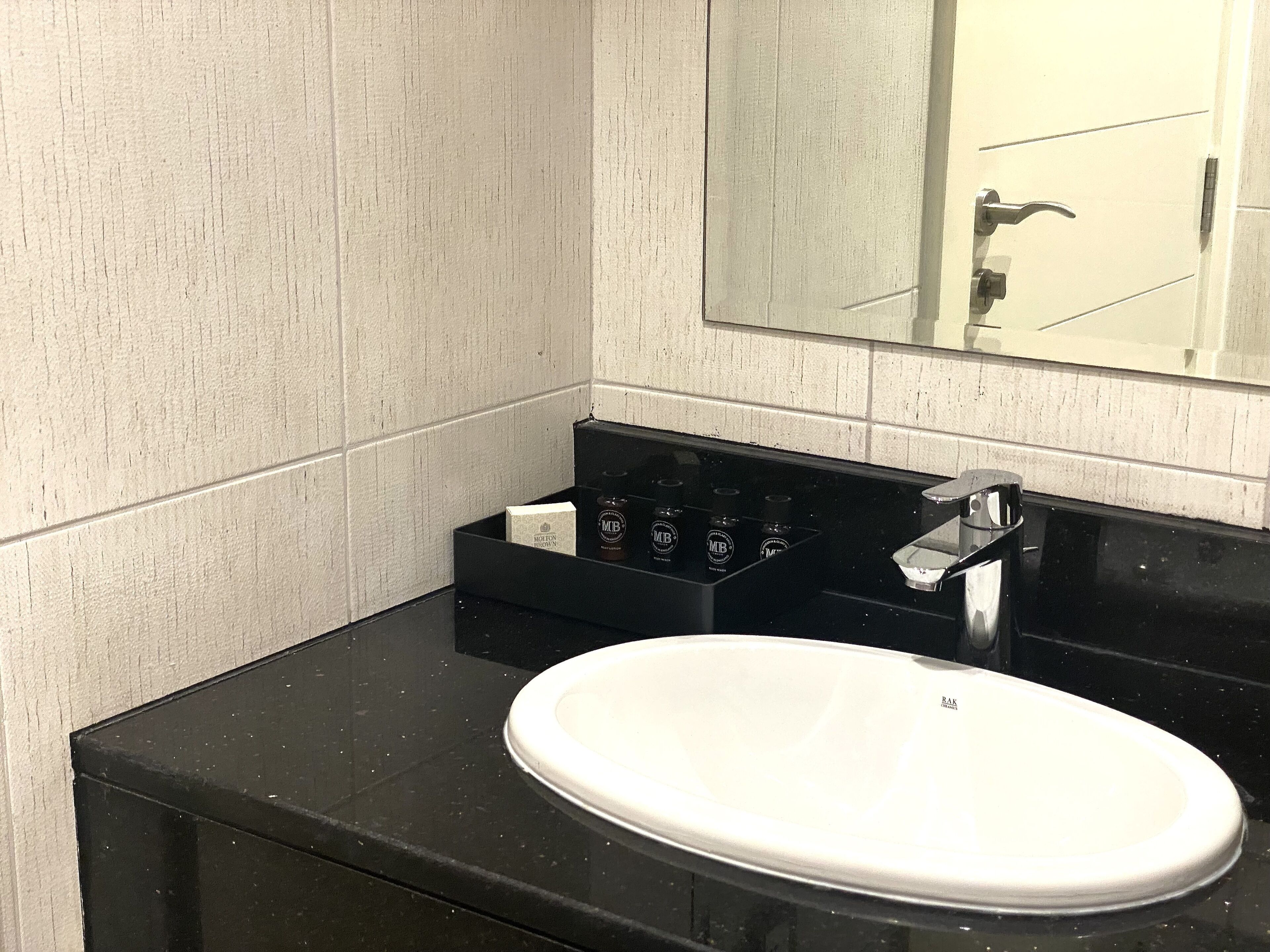Une salle de bain avec un lavabo blanc, un plan de toilette noir et un miroir au-dessus.
